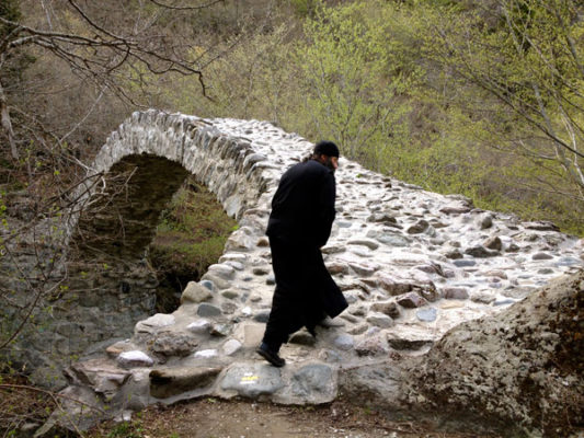 Georgian monk walks across medieval Rkoni single-arch "Tamar" bridge near Rkoni Monastery, Georgia. Seen on John Graham Tours.