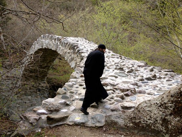 Georgian monk walks across medieval Rkoni single-arch "Tamar" bridge near Rkoni Monastery, Georgia. Seen on John Graham Tours.